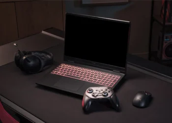 ستاپ گیمینگ شامل لپ‌تاپ گیمینگ با کیبورد RGB قرمز، کنترلر Xbox، ماوس گیمینگ و هدست روی میز در محیط نورپردازی تیره.