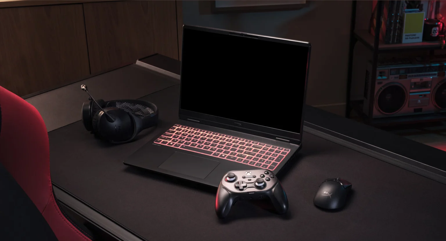 ستاپ گیمینگ شامل لپتاپ گیمینگ با کیبورد RGB قرمز، کنترلر Xbox، ماوس گیمینگ و هدست روی میز در محیط نورپردازی تیره.