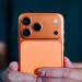 گوشی iPhone 17 Pro در رنگ نارنجی با ماژول دوربین بزرگ مستطیلی و سه لنز در گوشه بالا، روی پس‌زمینه‌ای ساده و روشن.