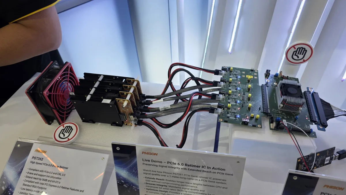 تجهیزات تست دمو زنده Phison PS7261 Retimer برای حفظ سلامت سیگنال در PCIe 6.0؛ اتصال کابل‌های نقره‌ای به برد اصلی و فن خنک‌کننده قرمز در کنار تابلو Live Demo