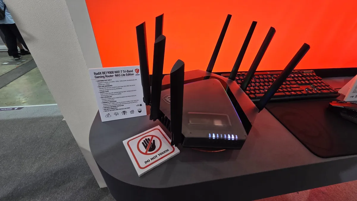 نمای نزدیک روتر گیمینگ MSI RadiX با بدنه مشکی و چند آنتن عمودی روی میز نمایشگاهی؛ کارت مشخصات محصول و برچسب Do Not Touch کنار دستگاه