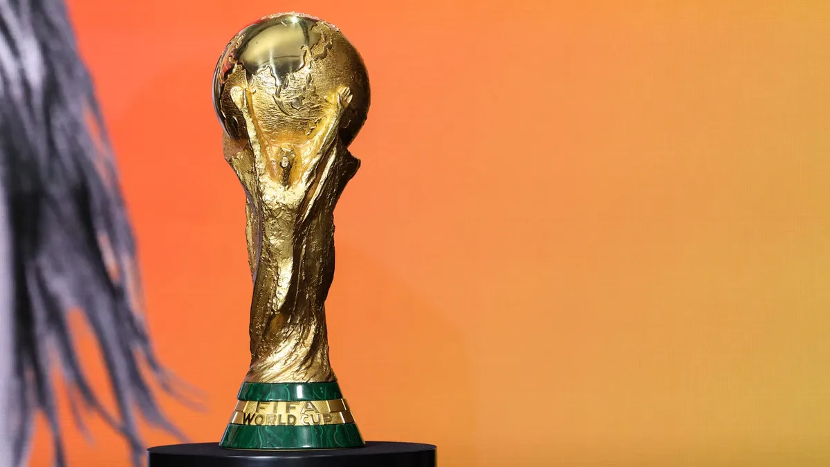 نمای نزدیک از جام طلایی جام جهانی فیفا (FIFA World Cup) در مقابل پس‌زمینه نارنجی و زرد ملایم