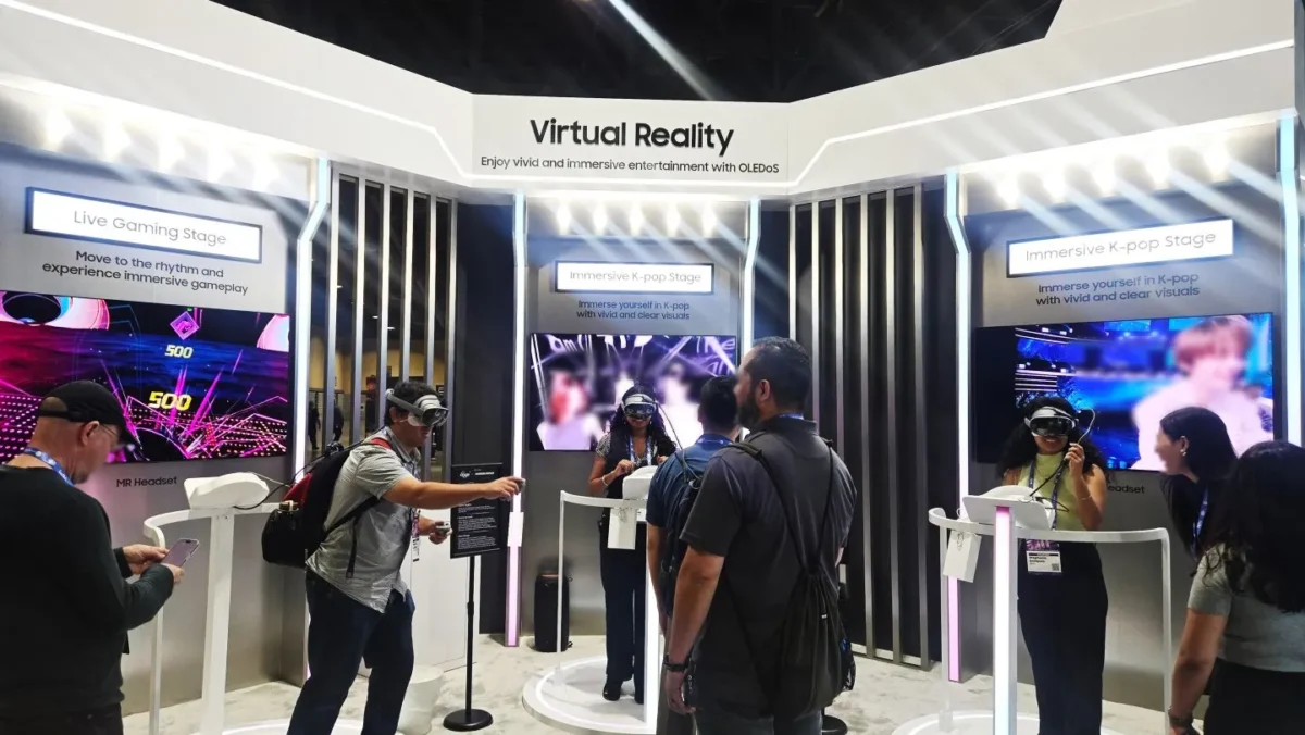 غرفه شرکت سامسونگ در یک نمایشگاه با تابلوی Virtual Reality، که بازدیدکنندگان در حال تست هدست‌های XR و تماشای محتوای Immersive K-pop و گیمینگ روی نمایشگرهای OLEDoS هستند.