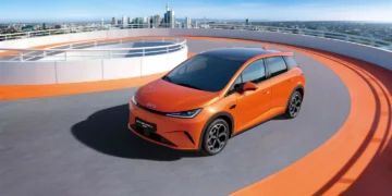 خودروی BYD Dolphin G DM-i در حال حرکت در مسیر شهری با چشم‌انداز ساختمان‌های مدرن در پس‌زمینه
