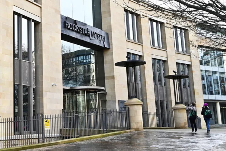 نمای بیرونی ساختمان مدرن و سنگی استودیو Rockstar North در ادینبرگ اسکاتلند با لوگوی بزرگ راکاستار نورث بالای ورودی چرخشی. عابران در حال عبور از مقابل نردههای حفاظتی ساختمان هستند