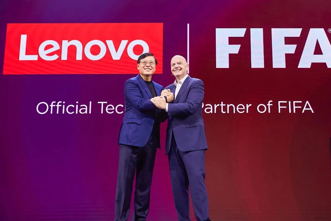 نمایندگان لنوو و فیفا در مراسم اعلام همکاری رسمی، مقابل لوگوهای Lenovo و FIFA روی صحنه ایستاده‌اند و با دست دادن توافق فناوری میان دو سازمان را نمایش می‌دهند.