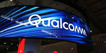تابلوی بزرگ Qualcomm روی نمایشگر LED منحنی در یک سالن نمایشگاهی با نورپردازی آبی؛ نمای غرفه و سقف سالن در پسزمینه