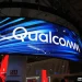 تابلوی بزرگ Qualcomm روی نمایشگر LED منحنی در یک سالن نمایشگاهی با نورپردازی آبی؛ نمای غرفه و سقف سالن در پسزمینه