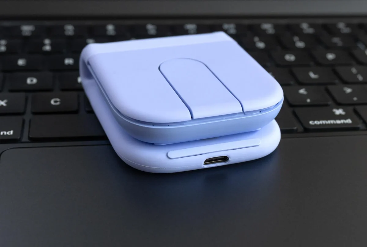 نمای نزدیک از ماوس بنفش تاشو که روی کیبورد لپتاپ قرار دارد. در این زاویه، پورت شارژ USB-C در قسمت جلویی دستگاه و لایههای سیلیکونی بدنه به وضوح دیده میشوند