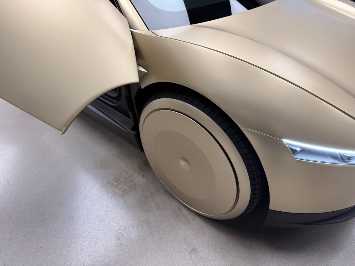 نمای نزدیک از چرخ آیرودینامیک و بخش جلوی بدنه Tesla Cybercab با درِ باز و طراحی یکپارچه پنلهای بدنه خودرو