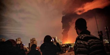 شهروندان در حال تماشای ستون عظیم دود و آتش ناشی از انفجار در یک منطقه شهری در شب
