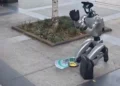 ربات انسان‌نمای Unitree G1 در خیابانی در شهر چنگدو چین روی زمین زانو زده و مقابل خود یک کد QR و ظرف دریافت کمک قرار داده است؛ یکی از رهگذران نیز در حال پرداخت پول و تعامل با این ربات است.