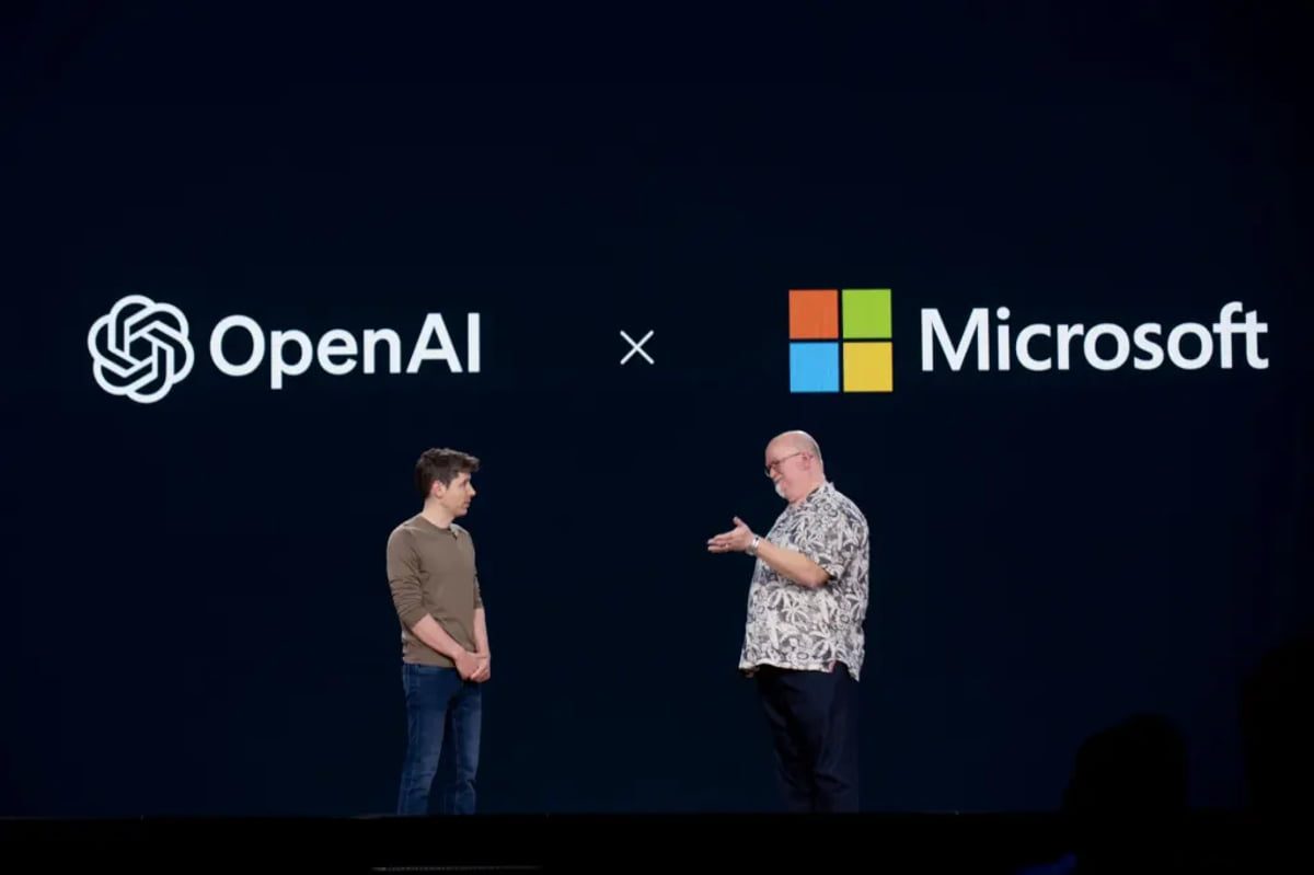 صحنهای از رویداد مشترک OpenAI و Microsoft با نمایش بزرگ لوگوهای دو شرکت روی پسزمینه تیره. دو نفر روی استیج ایستادهاند و در حال گفتوگو هستند، یکی در سمت چپ و دیگری در سمت راست