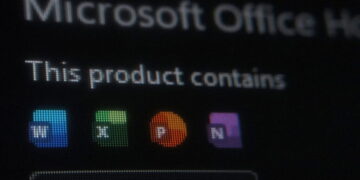 تصویر تاریک و خارج از فوکوس (Bokeh) از صفحه نمایش که عنوان نارنجی رنگ “Office” و متن کمرنگ “Microsoft Office Home and Stud” را در بخش بالایی آیکونهای برنامههای آفیس نشان میدهد.