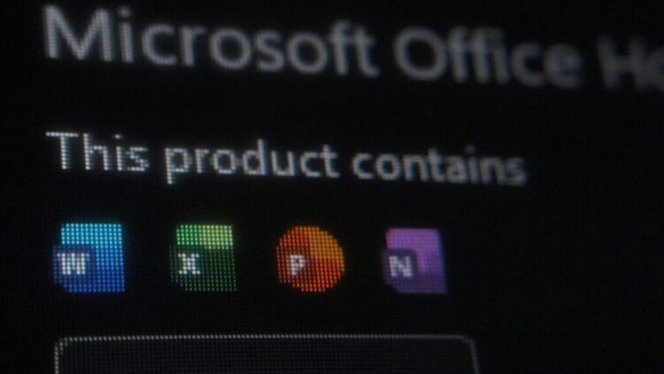 تصویر تاریک و خارج از فوکوس (Bokeh) از صفحه نمایش که عنوان نارنجی رنگ “Office” و متن کمرنگ “Microsoft Office Home and Stud” را در بخش بالایی آیکونهای برنامههای آفیس نشان میدهد.