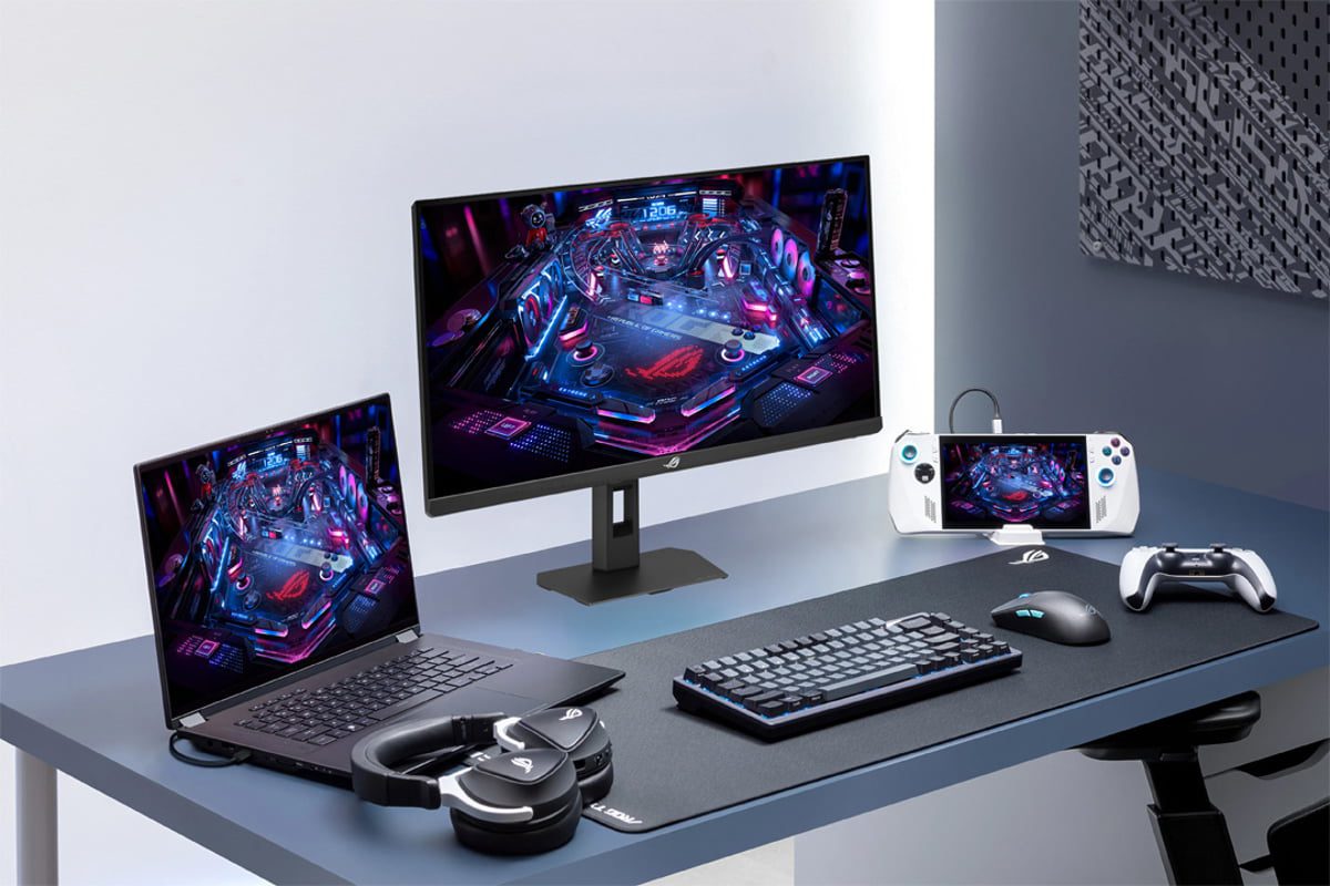 میز گیمینگ مجهز به لپتاپ، مانیتور ASUS ROG، کنسول دستی ROG Ally، کیبورد، ماوس، هدست و کنترلر؛ نمایشگرها یک بازی پینبال رنگارنگ را نشان میدهند