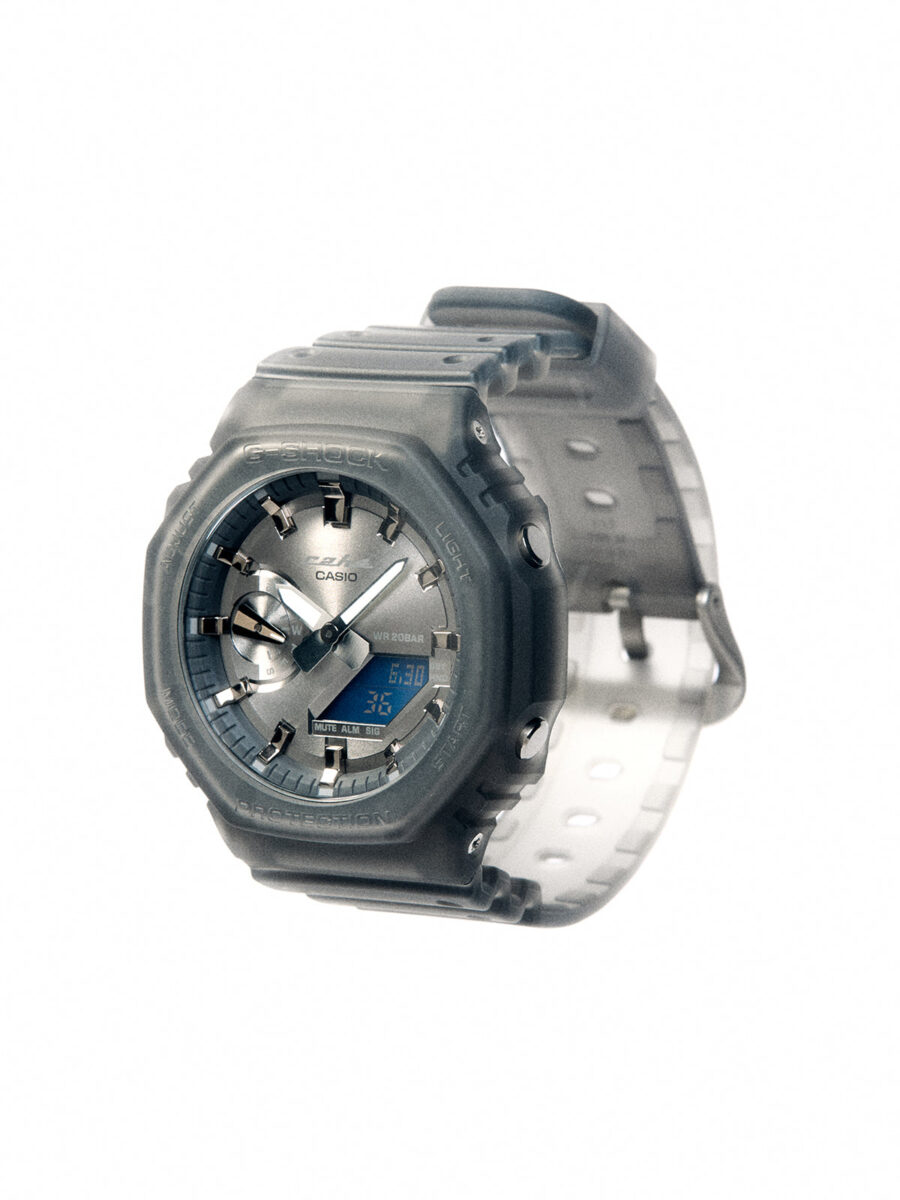نمای نزدیک ساعت مچی Casio G-Shock GA-2100 همکاری C2H4 با قاب هشت ضلعی دودی نیمه شفاف، صفحه خاکستری متالیک و نمایشگر دیجیتال آبی رنگ.