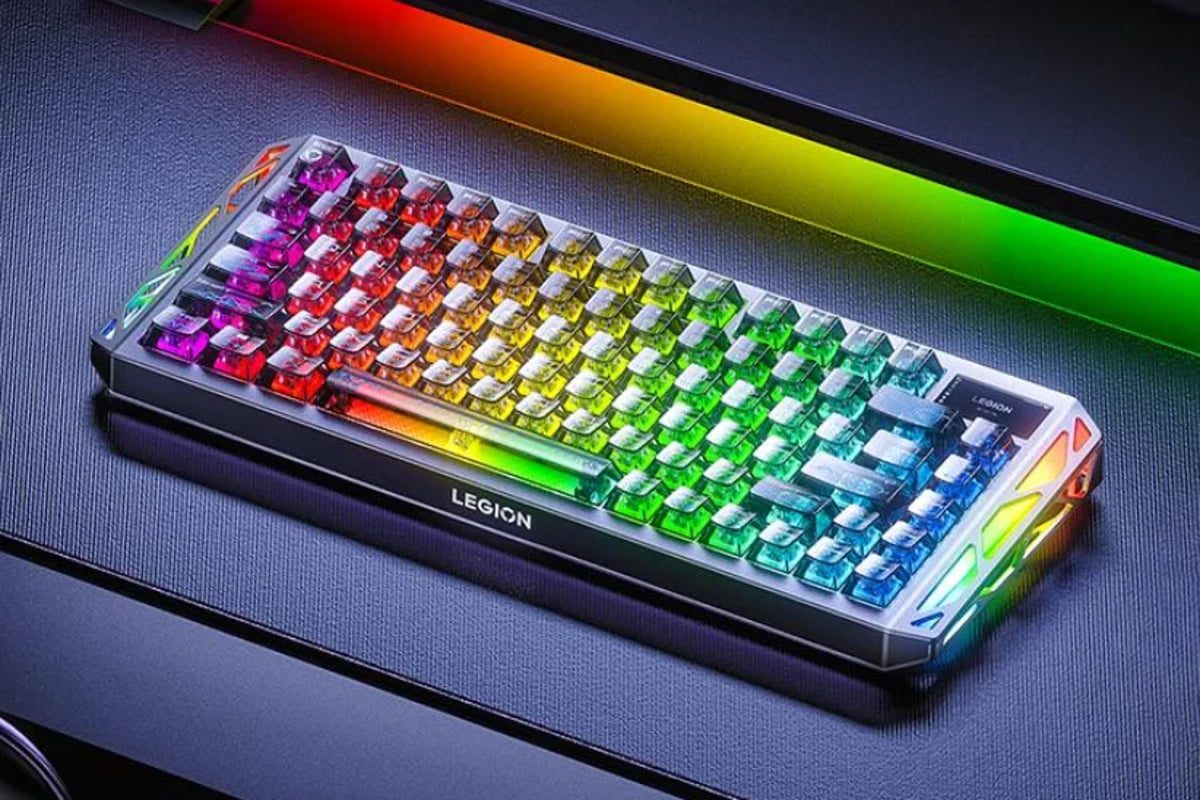 رندر تبلیغاتی از یک کیبورد مکانیکی گیمینگ Lenovo Legion با نورپردازی RGB تمام رنگی؛ کلیدهای شفاف با طیف رنگی از بنفش و قرمز تا سبز و آبی روشن دیده میشوند و بدنه کیبورد روی سطحی تیره با نوار نورانی رنگین کمانی در پس زمینه قرار گرفته است