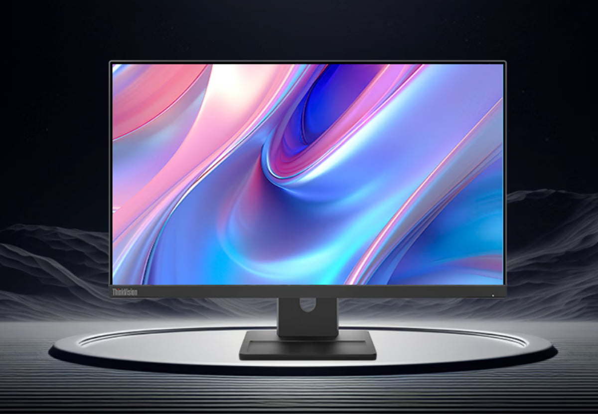 مانیتور Lenovo ThinkVision با حاشیه باریک و پایه مرکزی که روی صفحه آن طرحی انتزاعی از امواج رنگی آبی، بنفش و صورتی نمایش داده شده و روی سکویی دایرهای در فضایی تیره قرار دارد.
