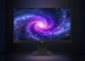مانیتور مشکی Lenovo ThinkVision روی پایه مشکی با نمایش تصویری از یک کهکشان مارپیچی بنفش، صورتی و آبی روی صفحه، در پسزمینهای تیره با هاله نوری ملایم.