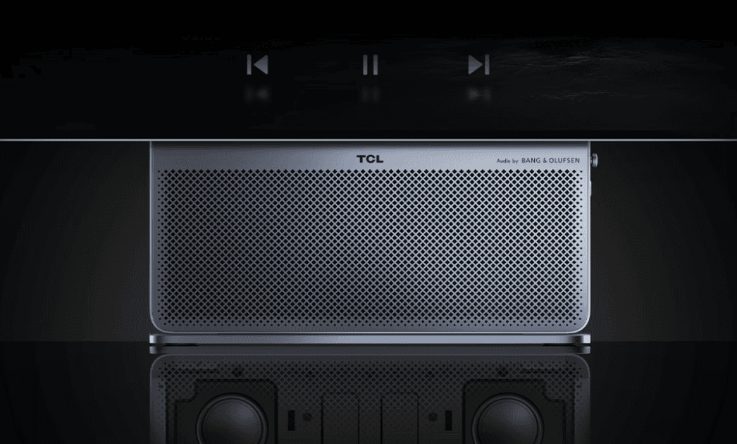نمای بسیار نزدیک از پایه مانیتور TCL با گریل اسپیکر فلزی سوراخدار و درج عبارت Audio by BANG & OLUFSEN. در انعکاس سطح زیرین، ساختار درایوهای اسپیکر دیده میشود و آیکونهای لمسی کنترل مالتیمدیا در پایین صفحه نمایش شناور هستند.