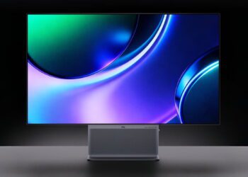 نمای روبروی مانیتور حرفه‌ای TCL با صفحه نمایش بزرگ و بدون حاشیه که والپیپر انتزاعی با طیف رنگی بنفش، آبی و سبز را نشان می‌دهد. در پایه مانیتور، اسپیکر شبکه‌ای با نشان برند صوتی Bang & Olufsen و لوگوی TCL خودنمایی می‌کند.