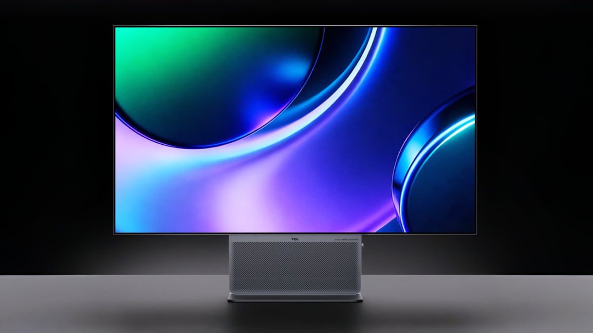 نمای روبروی مانیتور حرفه‌ای TCL با صفحه نمایش بزرگ و بدون حاشیه که والپیپر انتزاعی با طیف رنگی بنفش، آبی و سبز را نشان می‌دهد. در پایه مانیتور، اسپیکر شبکه‌ای با نشان برند صوتی Bang & Olufsen و لوگوی TCL خودنمایی می‌کند.
