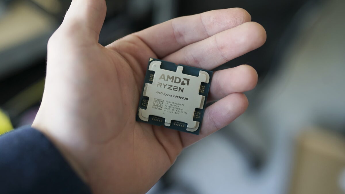 نمای نزدیک از یک پردازنده مربعی شکل AMD Ryzen 7 9850X3D که روی کف دست یک فرد قرار دارد. پخشکننده حرارت فلزی (IHS) با طراحی نمادین پایههای اختاپوسی شکل ایامدی دیده میشود که روی آن برند AMD RYZEN و شماره مدل به همراه پارت نامبر و بارکد دو بعدی حک شده است. پسزمینه تصویر به صورت فوکوس سطحی و محو است.