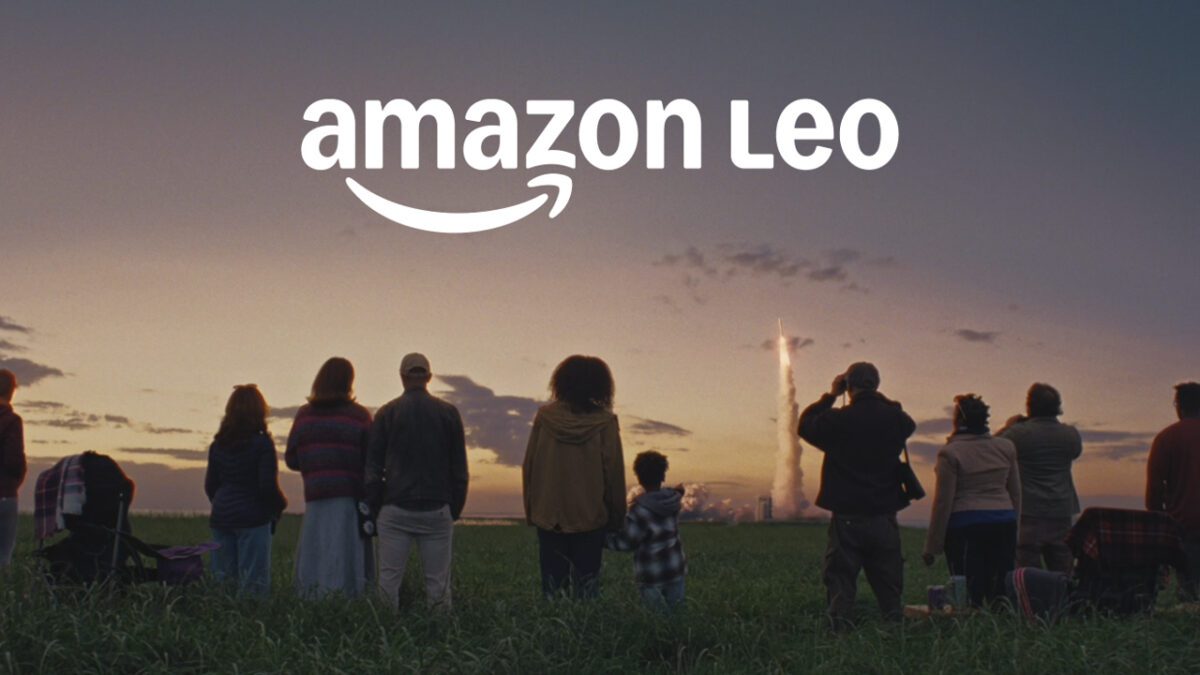 لوگوی Amazon Leo در آسمان هنگام پرتاب موشک حامل ماهواره، در حالی که گروهی از مردم پرتاب را تماشا می‌کنند؛ تصویری از پروژه منظومه ماهواره‌ای آمازون