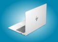 نمای پشت لپتاپ HP EliteBook نقرهای با لوگوی براق HP روی پسزمینه آبی، در حالت نیمهباز که بخشی از کیبورد و درگاههای سمت چپ آن دیده میشود