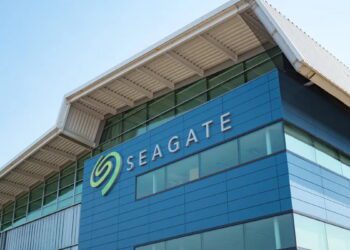نمای بیرونی مدرن از ساختمان اداری شرکت Seagate با نمای شیشه‌ای آبی‌رنگ و سقف فلزی با طراحی هندسی. لوگوی بزرگ و نمادین سیگیت با رنگ سبز در گوشه ساختمان درج شده که به عنوان تصویر مرجع برای اخبار شرکتی و معرفی پایگاه‌های توسعه سخت‌افزار کاربرد دارد.