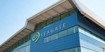 نمای بیرونی مدرن از ساختمان اداری شرکت Seagate با نمای شیشهای آبیرنگ و سقف فلزی با طراحی هندسی. لوگوی بزرگ و نمادین سیگیت با رنگ سبز در گوشه ساختمان درج شده که به عنوان تصویر مرجع برای اخبار شرکتی و معرفی پایگاههای توسعه سختافزار کاربرد دارد.