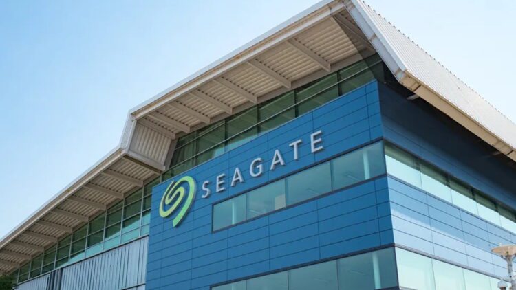 نمای بیرونی مدرن از ساختمان اداری شرکت Seagate با نمای شیشه‌ای آبی‌رنگ و سقف فلزی با طراحی هندسی. لوگوی بزرگ و نمادین سیگیت با رنگ سبز در گوشه ساختمان درج شده که به عنوان تصویر مرجع برای اخبار شرکتی و معرفی پایگاه‌های توسعه سخت‌افزار کاربرد دارد.