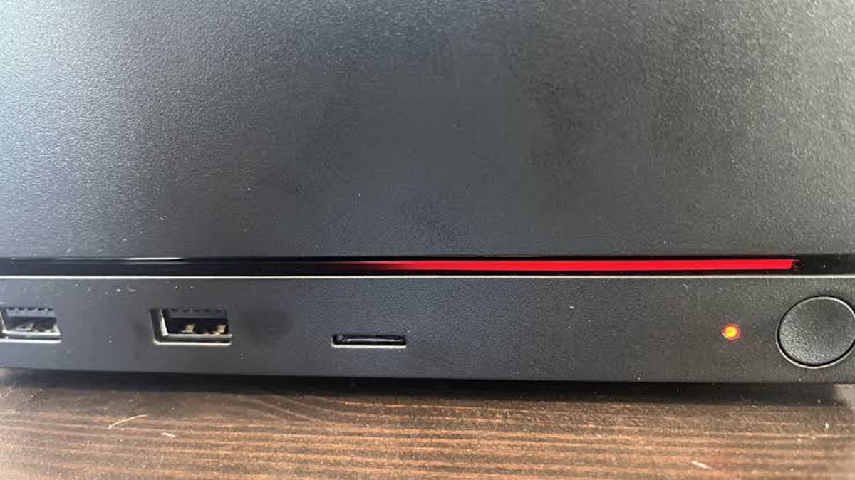 بخش جلویی یک دستگاه الکترونیکی سیاه که روی میز چوبی قرار دارد. دو پورت USB-A، یک پورت USB-C، چراغ وضعیت ریز نارنجی، دکمه پاور دایره‌ای و یک خط LED قرمز باریک و درخشان در شیار بالای پورت‌ها دیده می‌شود.