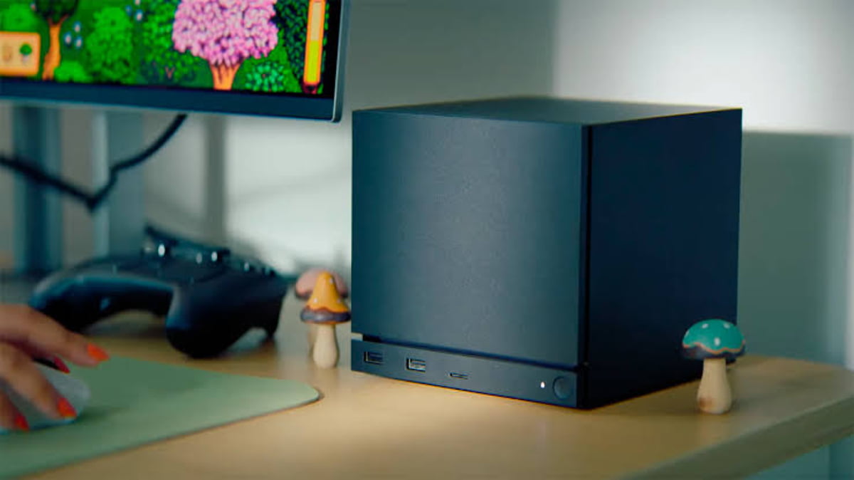 چیدمان میز کار یک گیمر شامل یک مینیپیسی (Mini PC) مدرن خاکستری تیره، ماوس و دسته بازی؛ در پسزمینه مانیتوری با بازی پیکسلی Stardew Valley و دو مجسمه قارچی تزیینی در کنار کیس قرار دارند