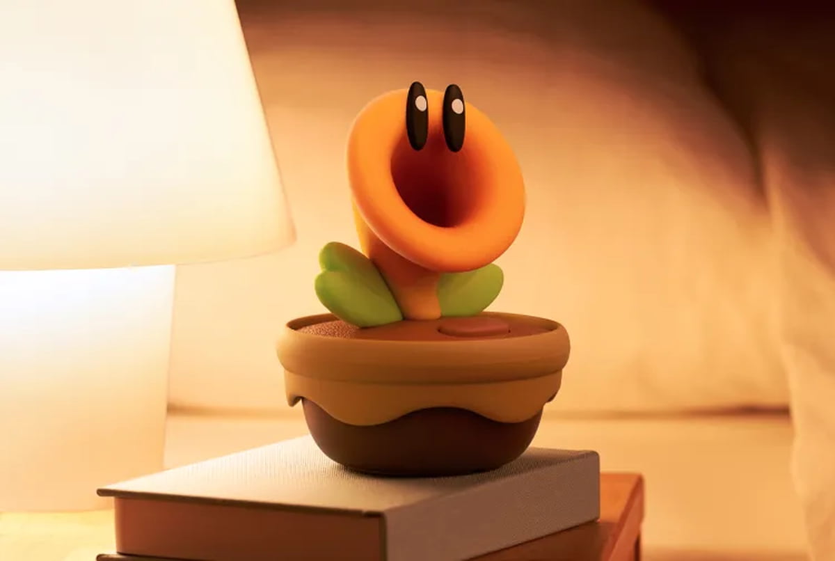 فیگور یا چراغخواب طرح “گل سخنگو” (Talking Flower) از بازی Super Mario Bros. Wonder که روی یک کتاب در کنار آباژوری با نور گرم قرار گرفته و فضایی دنج ایجاد کرده است.