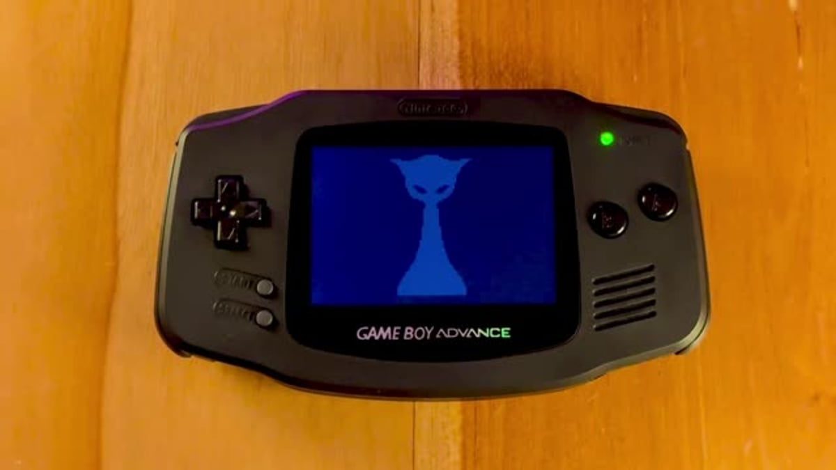 کنسول بازی مشکی Game Boy Advance روی سطحی چوبی قرار دارد و صفحهاش یک تصویر آبی با کاراکتری شبیه گربه را نشان میدهد