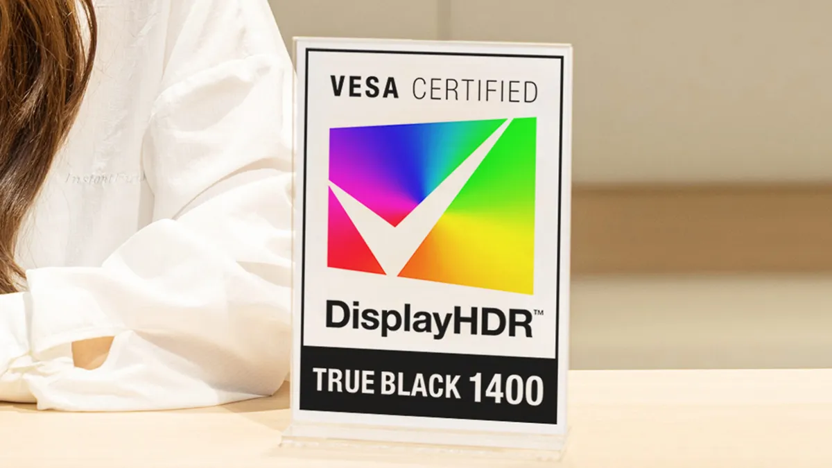 نشان رومیزی گواهی VESA DisplayHDR True Black 1400 با تیک سفید روی طیف رنگی، قرارگرفته روی میز کنار فردی با لباس سفید