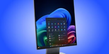 رندر تبلیغاتی کامپیوتر همهکاره لنوو (ThinkCentre AIO) با نمایشگر بدون حاشیه و نسبت تصویر عمودی که در محیط ویندوز ۱۱ قرار دارد؛ منوی استارت و اپلیکیشنهای پین شده در مرکز صفحه دیده میشوند و یک وبکم عریض در لبه بالایی دستگاه تعبیه شده است. کل دستگاه روی یک پایه فلزی تخت و مدرن با لوگوی لنوو در پسزمینهای با طیف رنگی آبی قرار گرفته است