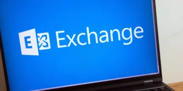 نمای نزدیک لپتاپ روی میز که لوگوی Microsoft Exchange را روی پسزمینه آبی نمایش میدهد.