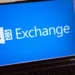 نمای نزدیک لپتاپ روی میز که لوگوی Microsoft Exchange را روی پسزمینه آبی نمایش میدهد.