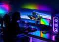 گیمر نشسته پشت میز گیمینگ با مانیتور بسیار عریض خمیده AOC AGON، نورپردازی نئونی RGB و کیس شفاف گیمینگ.