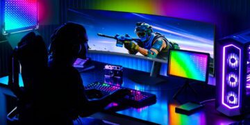 گیمر نشسته پشت میز گیمینگ با مانیتور بسیار عریض خمیده AOC AGON، نورپردازی نئونی RGB و کیس شفاف گیمینگ.