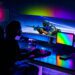 گیمر نشسته پشت میز گیمینگ با مانیتور بسیار عریض خمیده AOC AGON، نورپردازی نئونی RGB و کیس شفاف گیمینگ.
