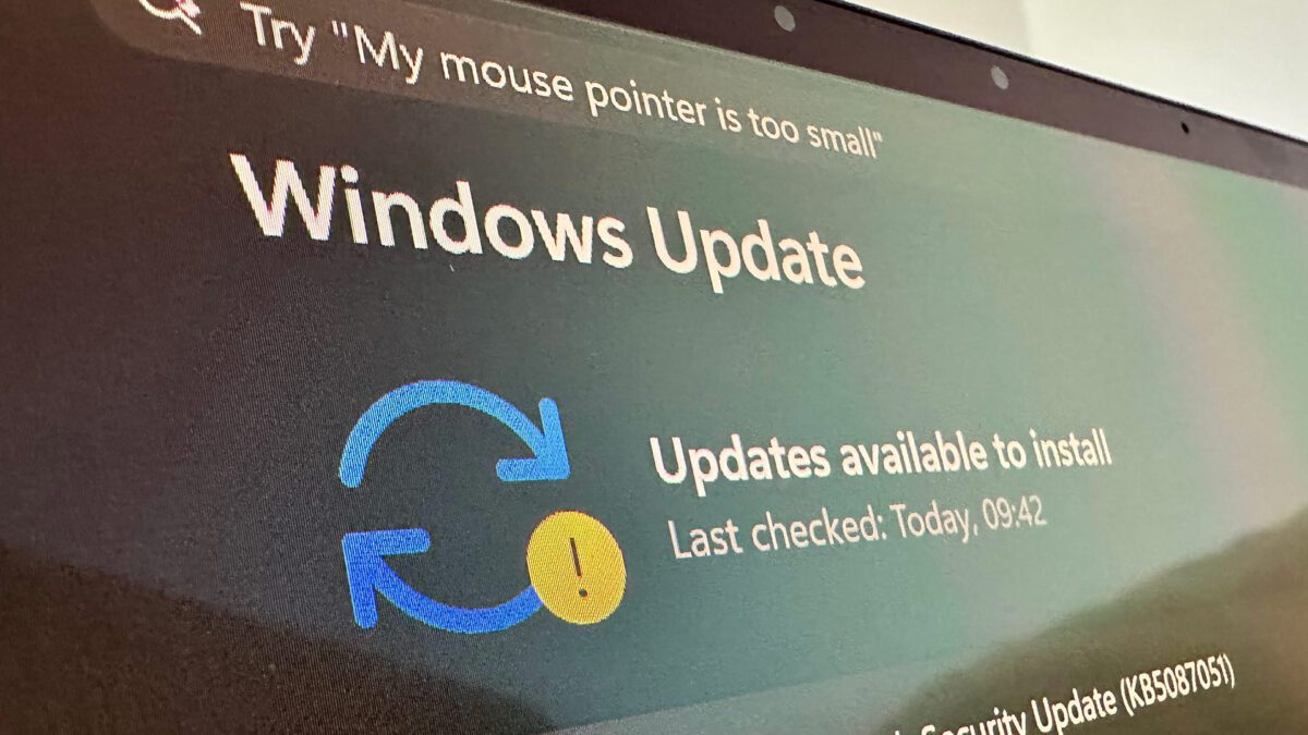 صفحه Windows Update روی مانیتور با آیکون فلشهای چرخان آبی، علامت تعجب زرد و پیام وجود بهروزرسانی برای نصب.