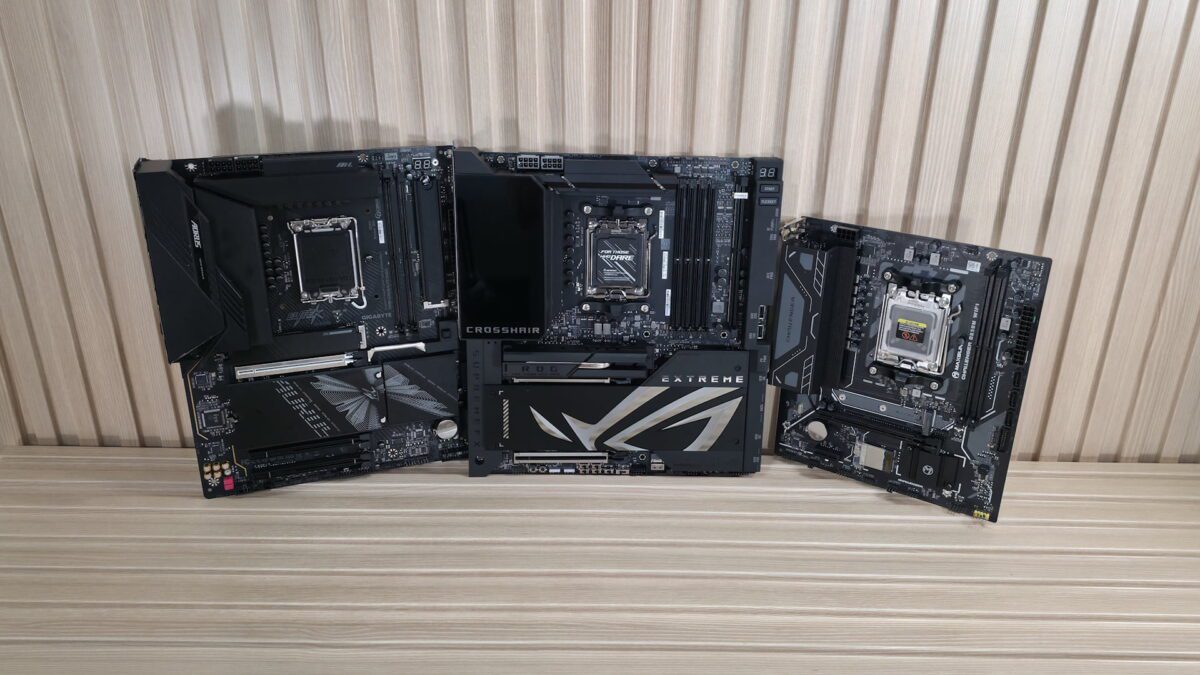 سه مادربرد مشکی ردهبالا از برندهای مختلف، شامل مدلهایی با نشانهای Aorus، ROG Crosshair و ROG Extreme، در برابر دیوار چوبی.