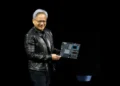 جنسن هوانگ (Jensen Huang)، مدیرعامل انویدیا، با کاپشن چرم مشکی روی صحنه در حال لبخند زدن و در دست داشتن یک برد مدار الکترونیکی پیشرفته و مادربورد سرور هوش مصنوعی.