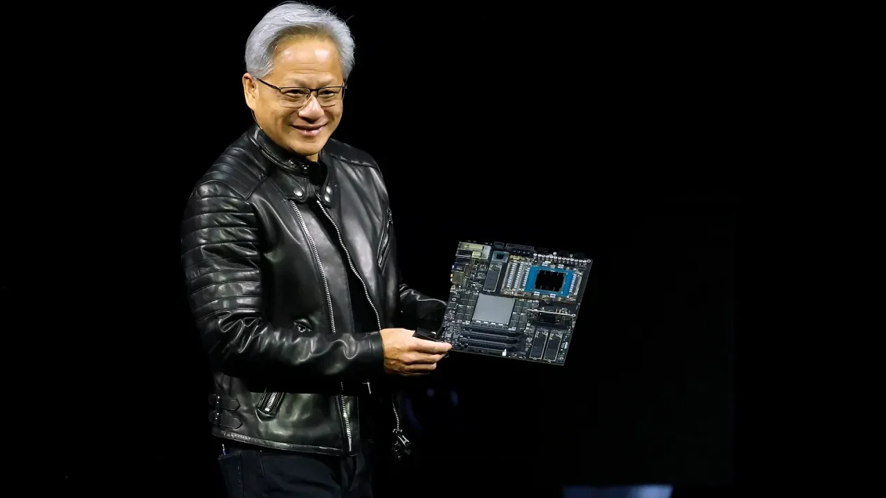 جنسن هوانگ (Jensen Huang)، مدیرعامل انویدیا، با کاپشن چرم مشکی روی صحنه در حال لبخند زدن و در دست داشتن یک برد مدار الکترونیکی پیشرفته و مادربورد سرور هوش مصنوعی.