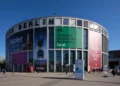 نمای بیرونی ساختمان مدور مرکز همایش‌های Messe Berlin با بنرهای تبلیغاتی بزرگ شرکت‌های هایر، اسنپدراگون و لوگوی نمایشگاه IFA در روز آفتابی.