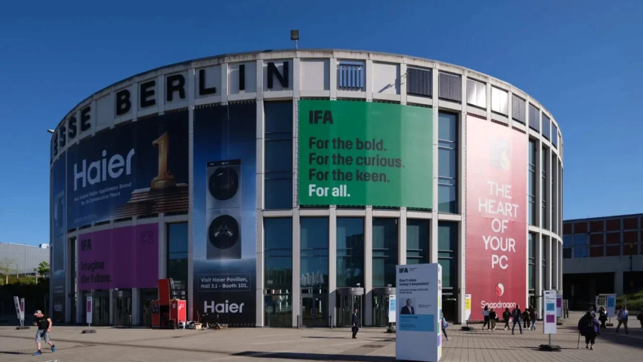 نمای بیرونی ساختمان مدور مرکز همایشهای Messe Berlin با بنرهای تبلیغاتی بزرگ شرکتهای هایر، اسنپدراگون و لوگوی نمایشگاه IFA در روز آفتابی.